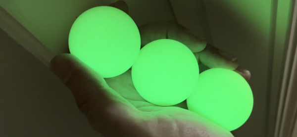 A hand holding three glowing green balls.